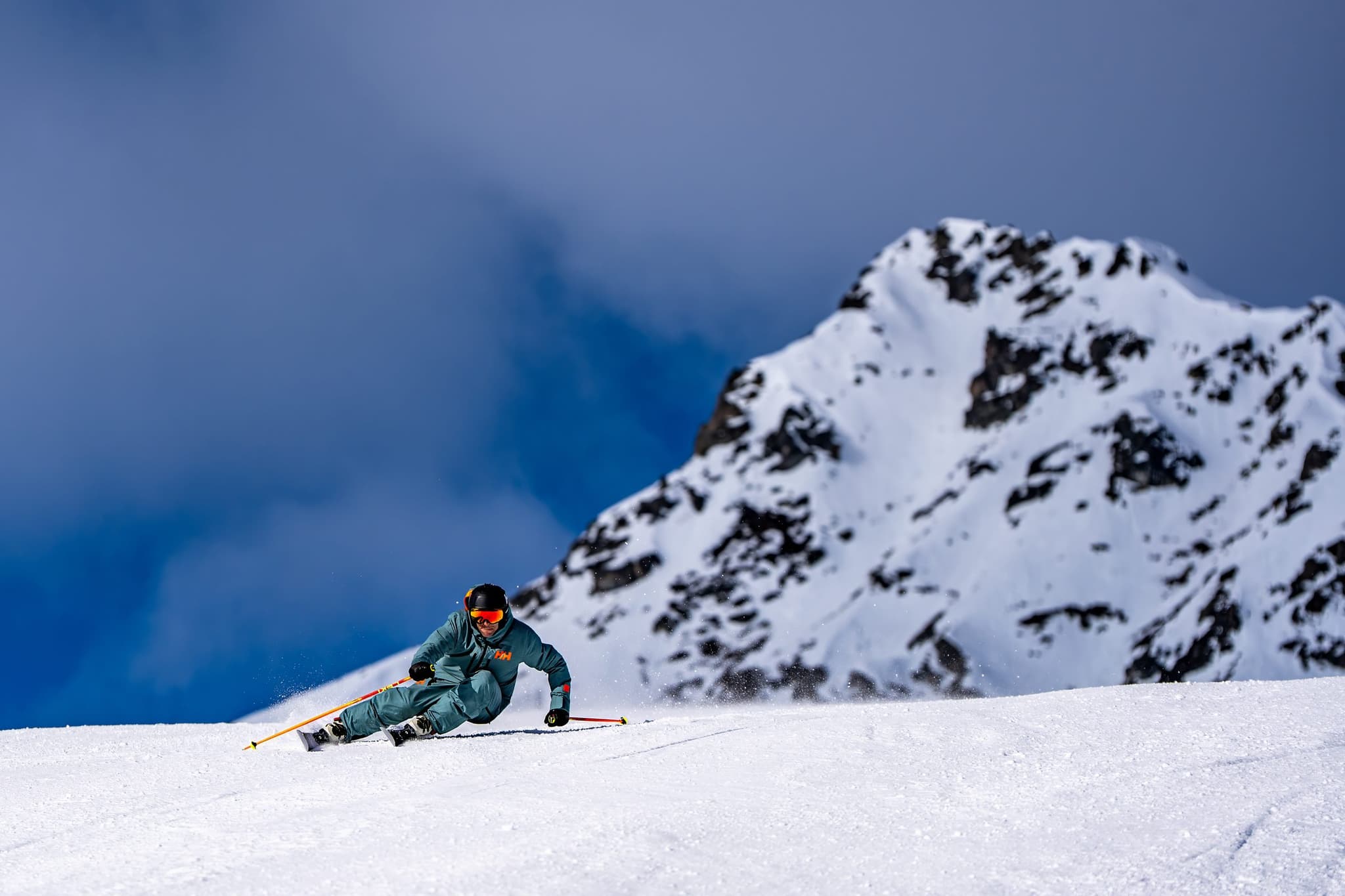 Skiløper carver i preparert bakke foran en snødekt fjelltopp