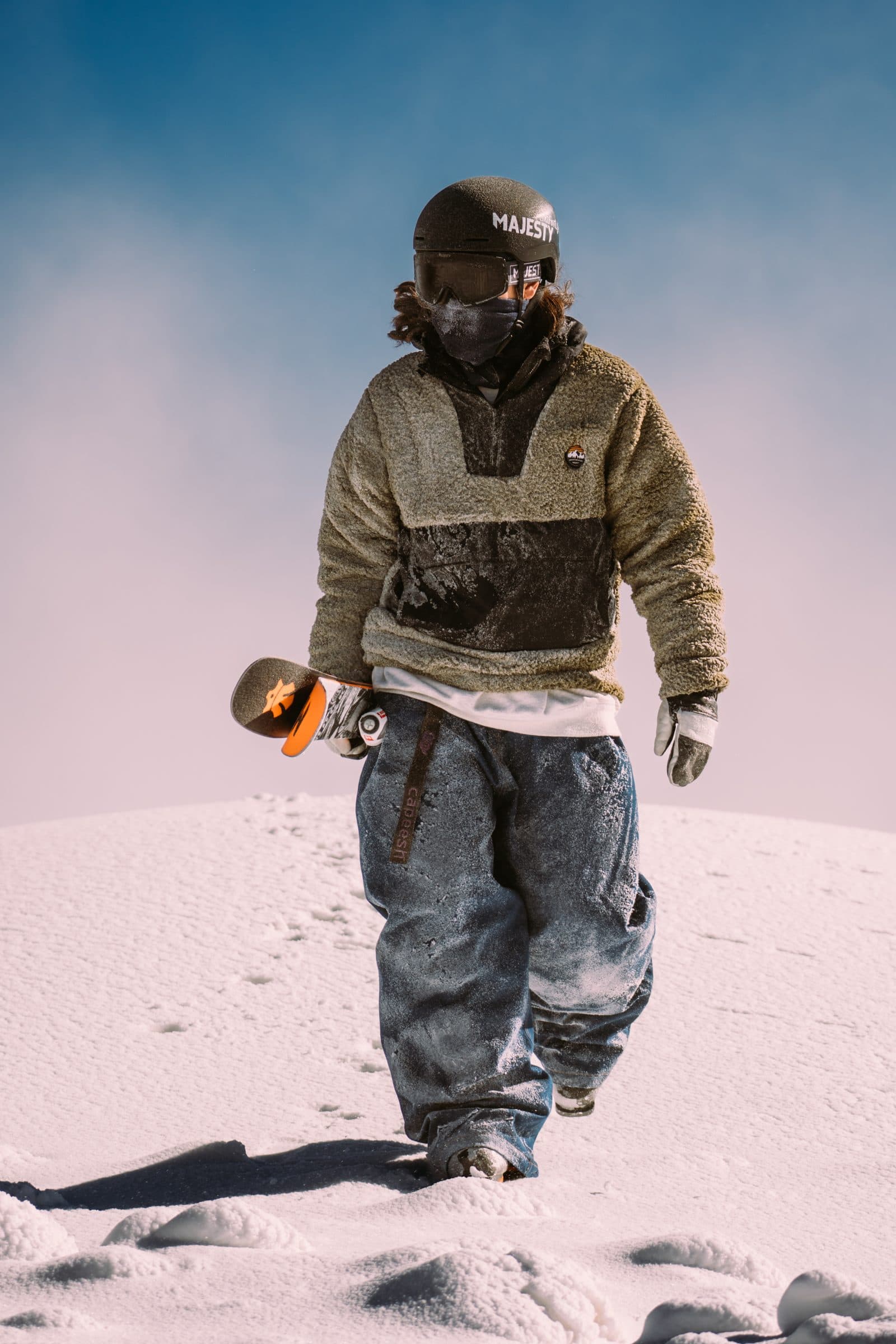 Freeskier med Majesty-hjelm går i snøen med twintipski under armen